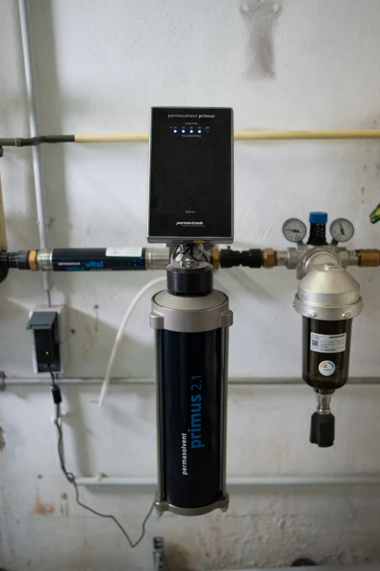 Eine Wasseraufbereitungsanlage mit schwarzem Behälter, Steuerkopf und transparentem Filter ist an Kupferrohre angeschlossen.