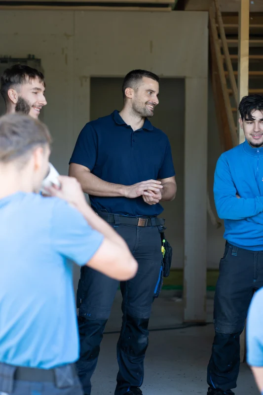 Mitarbeiter in blauen und dunklen Arbeitsoberteilen stimmen sich in einem noch unfertigen Innenraum ab.