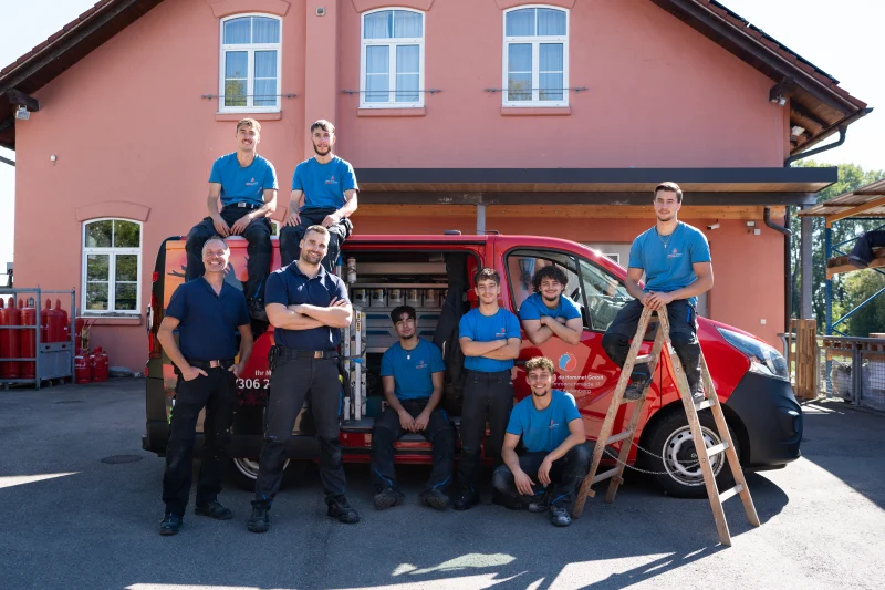Das Team von Zanker & du Hommet vor dem Firmengebäude mit roten Fahrzeugen.