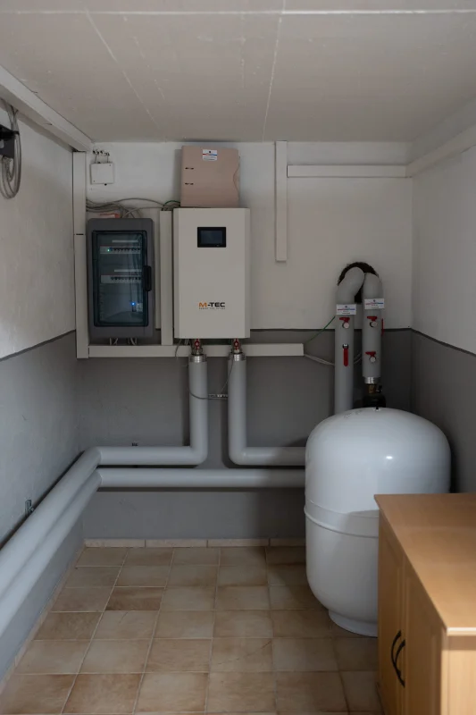 Eine weiße Wandregelung, Pumpengruppen mit Anzeigen und ein weißes Ausdehnungsgefäß sind im Technikraum installiert.